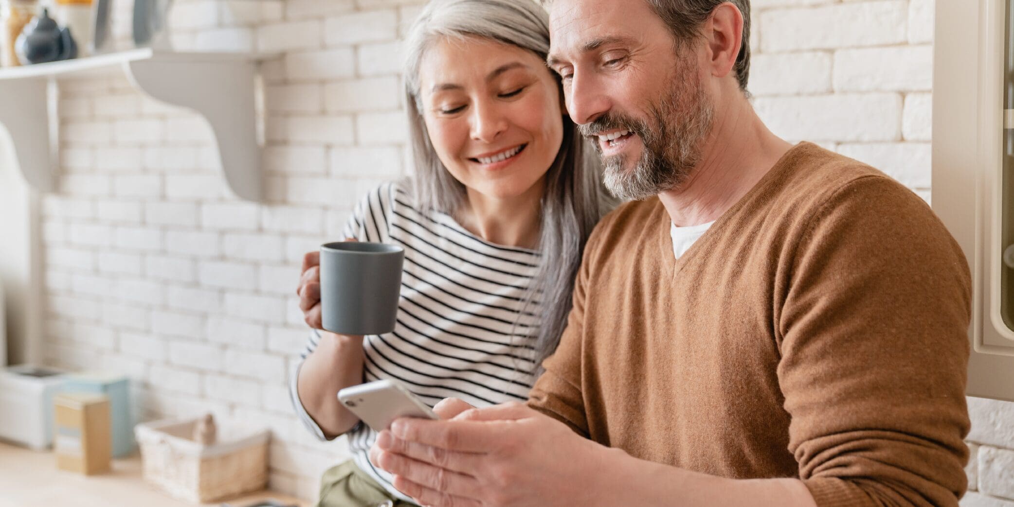 woman holding a mug while looking at man's cellphone screen
