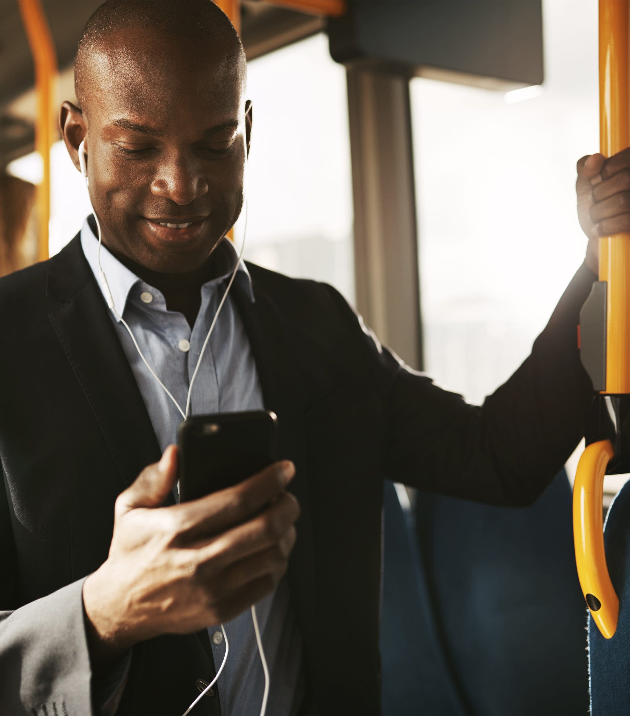 Smiling Businessman Wearing a Suit Standing on a Bus Looking at Smartphone With Earphones