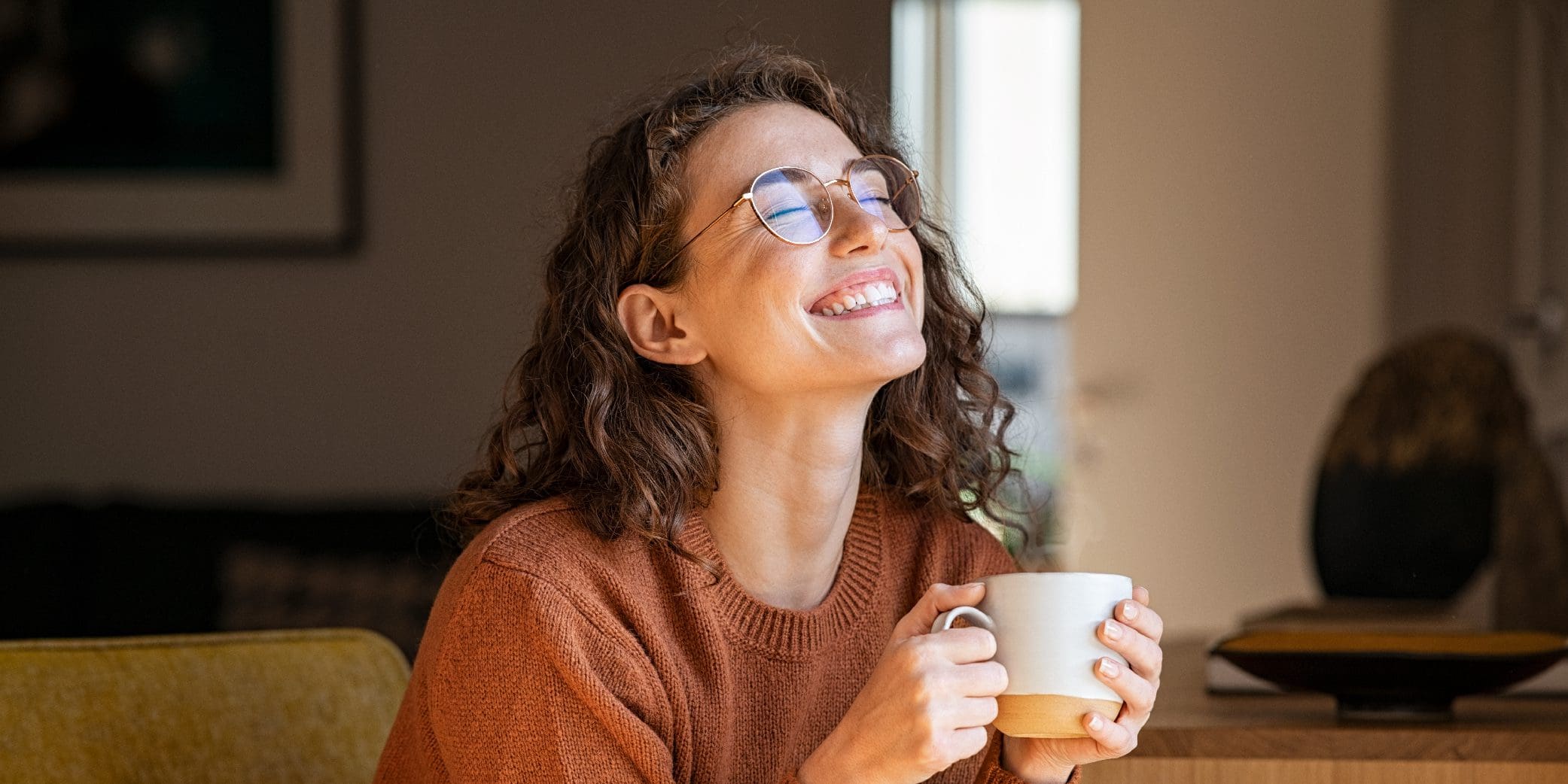 Joyful and Smiling Young Woman Enjoying a Cup of Coffee at Home
