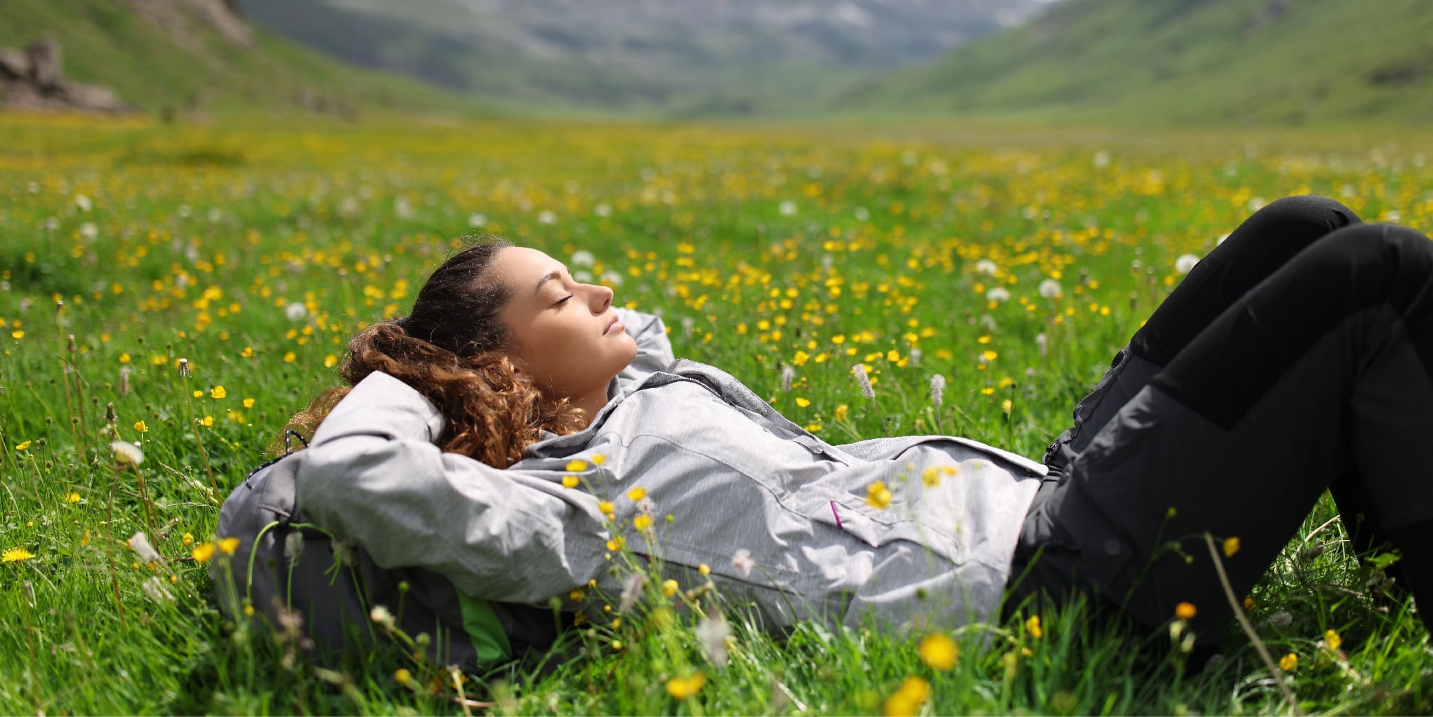 Girl laying on a grass field with flowers around.